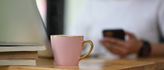 A coffee cup is putting on a wooden working desk over a woman as a background.