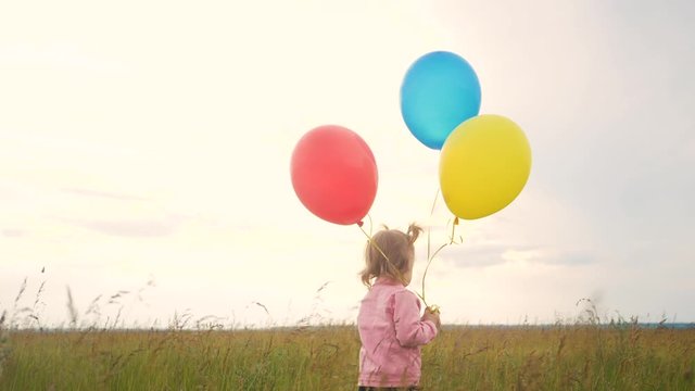 daughter little girl fun runs with balloons a on her birthday outdoors by field. dream happy family concept. child girl kid day. child is running lifestyle and balloons on a background of blue sky