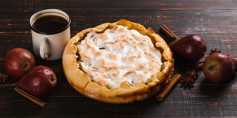 Pear pie with cream, homemade pastries on the wooden table, coffee and spices. Copy space.