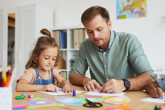 Portrait of young father drawing with little daughter while enjoying kindergarten class together