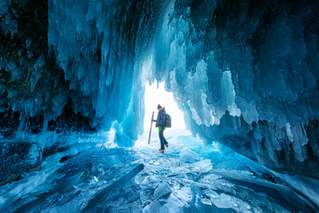 A tourist or photographer travels in the stunning ice cave on Lake Baikal, Russia. Winter blue background texture.