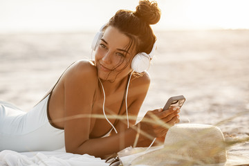 Woman in Bikini with a Smartphone and Headphones on the Beach