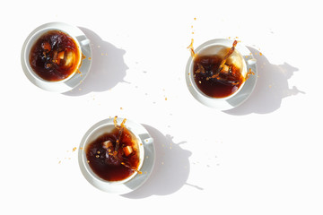 Black coffee in white cups, top view. Sugar lumps are thrown into the cup, spectacular splashes are spilling out of the cup. White background. International coffee day.