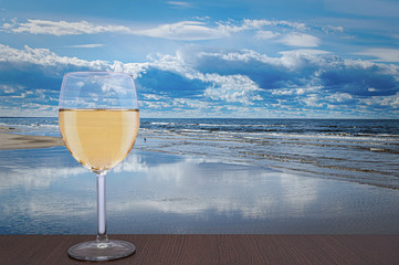 Glass of white wine against beautiful marine landscape. Baltic sea during sunny day with beautiful clouds with gulls in the waves in Jurmala, Latvia