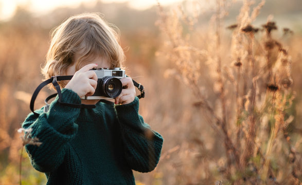 Small girl in autumn nature, taking photographs with camera.