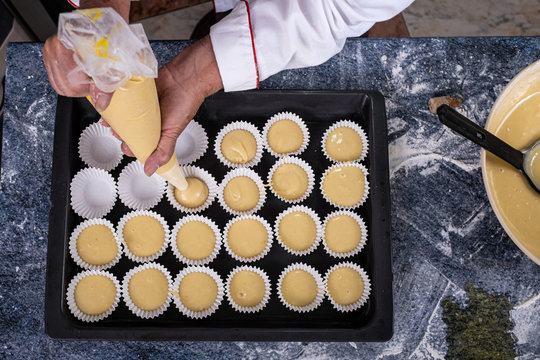 zenithal plane of a baker pouring pastry cream with a sleeve in a steel tray