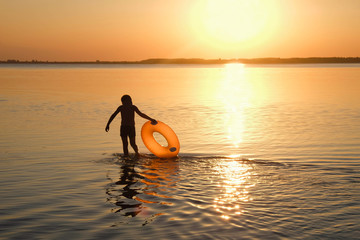 Silhouette of a boy with an orange inflatable circle. Sunset on Lake Svityaz in Ukraine. Copy space. 