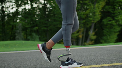 Female runner with artificial limb exercising in park.Girl legs running outdoors