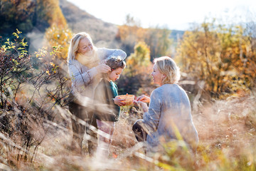 Small girl with mother and grandmother collecting rosehip fruit in autumn nature.