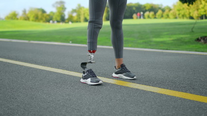 Jogger with artificial limb standing in park. Woman at start position on road
