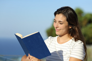Fototapeta premium Relaxed woman reading a book in a hotel balcony