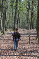 A mother with a small child in a sling on a dirt road through a beech grove. Ukraine