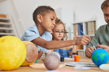 Side view portrait of cute African-American boy painting planet model while enjoying art and craft lesson in school or development center, copy space © Seventyfour