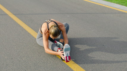 Handicapped girl stretching legs on road. Runner warming after workout