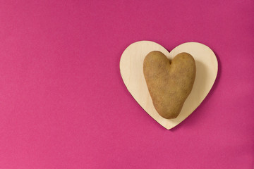 Ugly potatoes in the shape of a heart on a wooden board on a pink background. Unusual concept of vegetables or food waste. horizontal orientation. Top view. Copy space