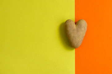 Ugly potato in the shape of a heart on a double green and orange background. Funny, unusual concept...