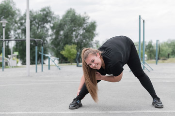 Fat young woman doing stretching exercises outdoors. Overweight girl makes bends before jogging.