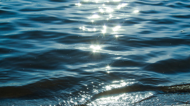 Sun glare in waves of sea water on a tropical beach in summer in nature close-up. Beautiful texture of water waves.Sea wave and sand seashore. Golden sun light over the sea ocean waves.