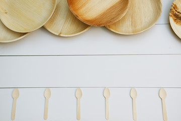 Platos de bambú y cucharas de madera sobre fondo de tablas blancas vistas desde arriba.
