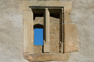 Window from two parts of an old brown castle, reveals a window with a blue sky. Stetten, Germany