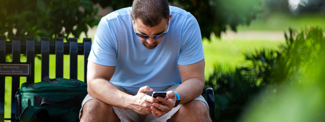 man texting on his phone sitting on a bench in winter garden park in orlando florida on the rose...