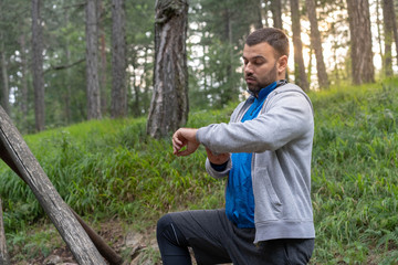 Young man in blue sports wear stretching in forest before running. Looking at his sports watch.