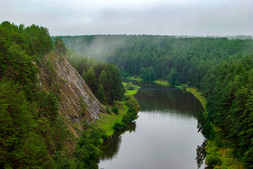 Fototapeta premium Beautiful river landscape with forest slopes of mountains. Limestone rocks in the Ural mountains. Cloudy sky in the background.
