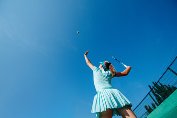 Low angle shot of a teenage girl playing tennis, throwing ball up and serving