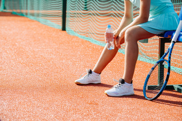 Legs of a girl sitting on a chair bench next to tennis court to take short break