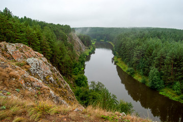 Beautiful river landscape with forest slopes of mountains. Limestone rocks in the Ural mountains. Cloudy sky in the background.