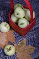 Apples in a red wicker basket. Nearby are apples and dried maple leaves. Fruit harvest.
