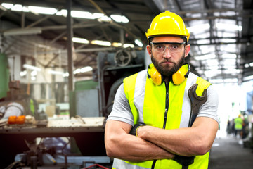 Portrait of industrial engineer worker wearing helmet and safely glasses standing with arms crossed, holding wrench and working at manufacturing plant factory, young man working in industry