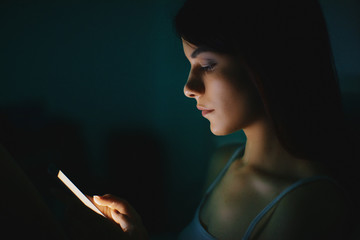 Obraz premium Young beautiful womanl in bed using mobile phone late at night at dark bedroom, internet addiction concept