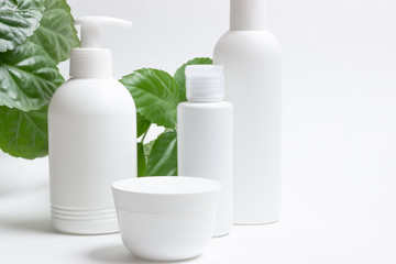 Set of cosmetic cans of organic cosmetics for face and body care on a white background with green leaves. Cream, shampoo and lotion on a light background. Layout, copy space.