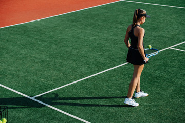 Slim teenage girl walking on a new tennis court, bouncing ball off her racket
