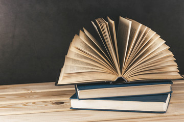 Old books on wooden shelf. Open book with hardback, fanned pages. Home library. Horror story. Vintage literature. Back to school. Education background. Copy space for text.