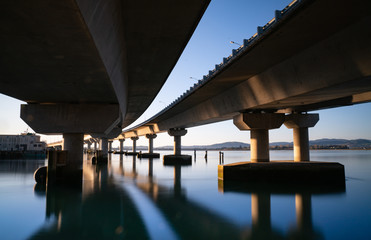 Sweeping structural lines of Tauranga Harbour Bridge from below over calm blue water