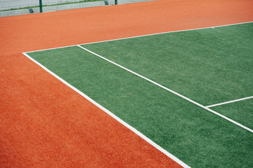 Corner of a green inner tennis court with white markings and brown outer part