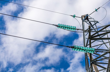 Close up of a transparent turquoise high voltage insulator or isolator in sunlight on electric tower on blue sky background.