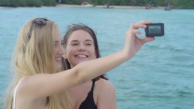 Beautiful two young woman in bikini selfie on tropical beach in vacation, taking a photo on smartphone with enjoy and fun in holiday, girl with friend and friendship to travel trip in summer.