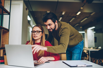 Shot of business man and woman looking at computer monitor and reading news, focused team working together in office while feeling shock of receiving message from friend at laptop application indoors