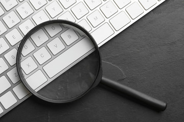 Magnifier glass and keyboard on black slate background, flat lay. Find keywords concept