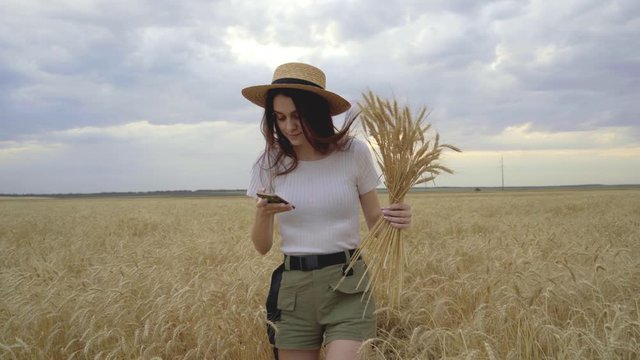 A girl in a straw hat takes pictures of herself in a wheat field.