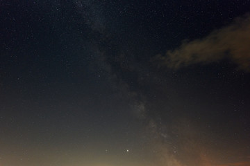 Milky way in the night sky with orange nebula, the planet Jupiter and the constellation Swan can be seen. August.
