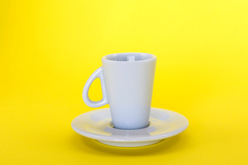 A white espresso cup and saucer with an upside down handle on a yellow background