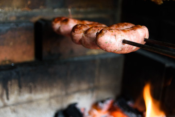 Linguiça sendo assada na churrasqueira. Churrasco feito em casa tradicional no sul do Brasil. Vista lateral: linguiça, carvão e fogo. 