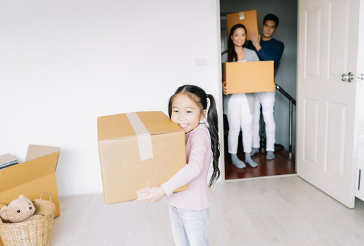Portrait of a happy asian little daughter carrying boxes into the a new home on moving day. Happy Family move on a new home concept, helping parents with belongings, mortgage and relocation.