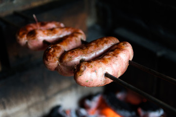 Linguiça sendo assada na churrasqueira. Churrasco feito em casa tradicional no sul do Brasil. Vista superior: linguiça, carvão e fogo. 
