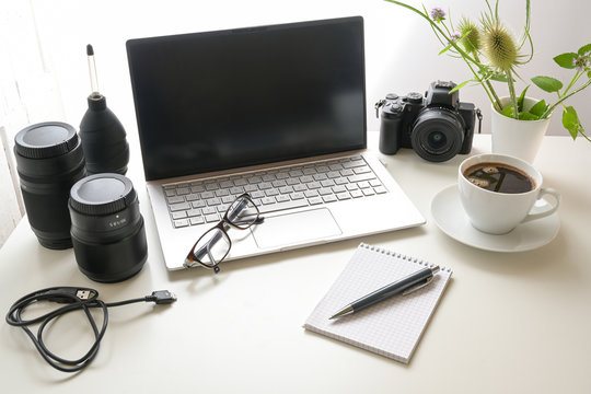 Workplace of a photographer, white office desk with laptop, camera, equipment, notepad and a cup of coffee, copy space, selected focus