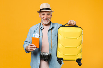 Smiling traveler tourist elderly gray-haired man in hat photo camera isolated on yellow background. Passenger traveling abroad on weekends getaway. Air flight journey. Hold passport tickets suitcase.